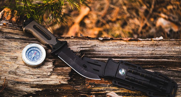 Hunting knife and compass on a log in the autumn forest