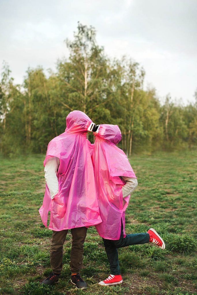 A vertical closeup shot of two people in pink plastic raincoats and VR headset kissing each other